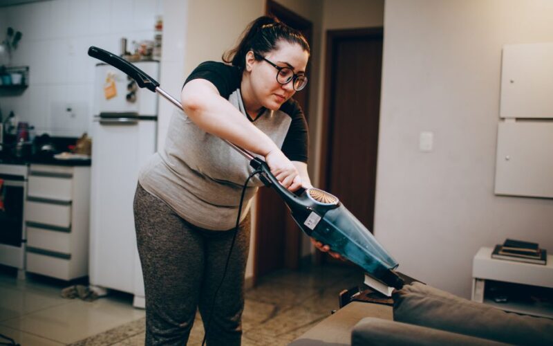 A woman vacuuming a couch in a cozy living room setting, emphasizing daily housework.