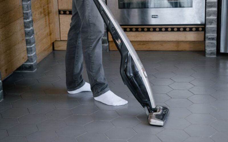 A person cleaning a tiled floor with a modern vacuum cleaner indoors.