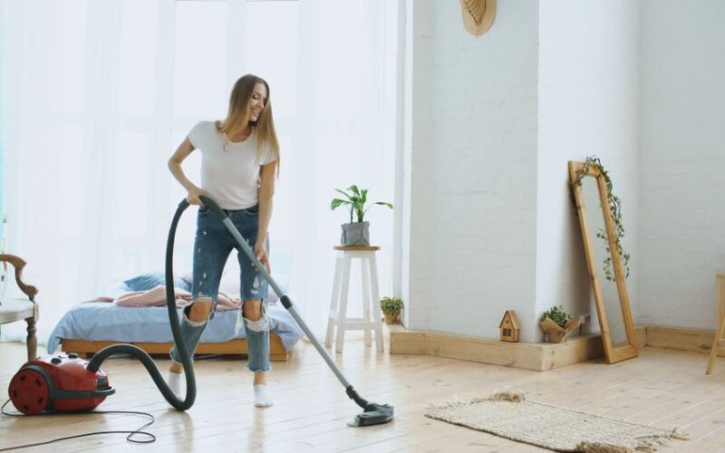Young woman cleaning her bedroom with a vacuum cleaner, enjoying the tidy space.