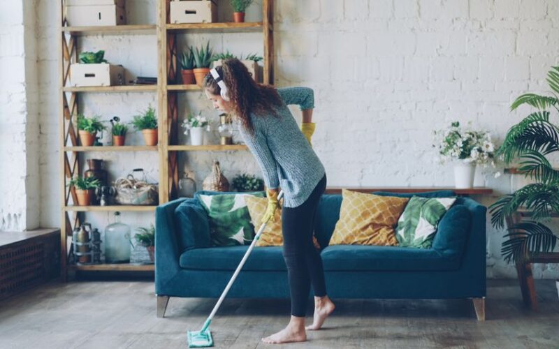A woman cleaning a stylish living room with a mop, surrounded by plants and decor.