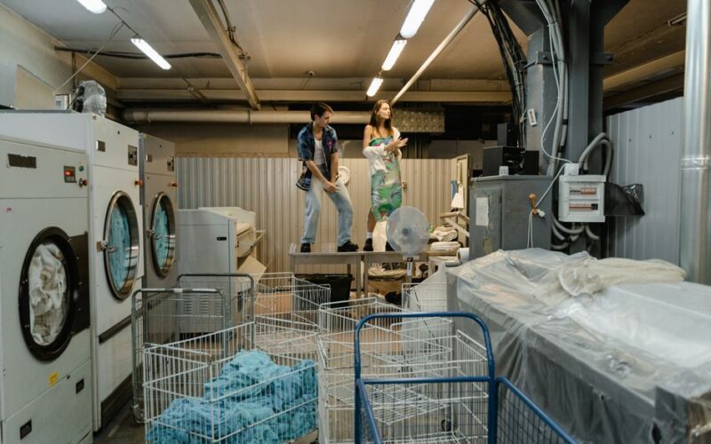 Two people take a break in a busy industrial laundry facility, surrounded by machines and laundry carts.