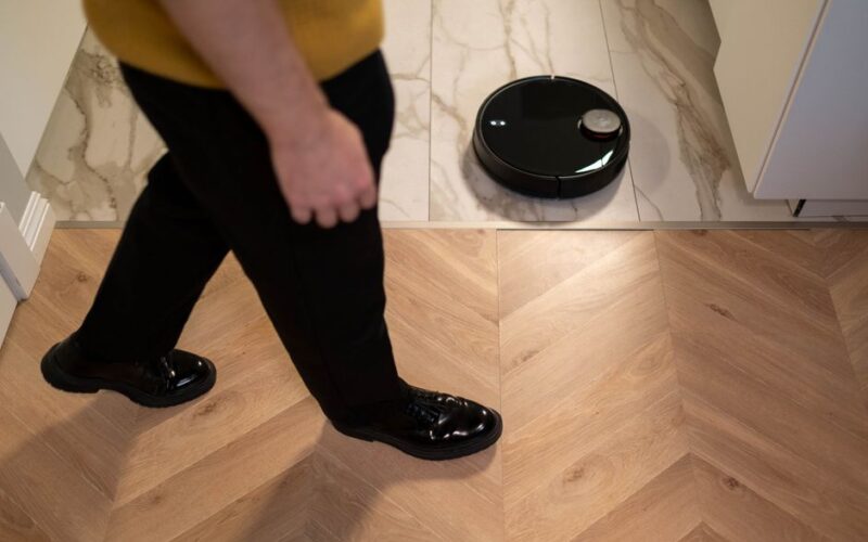 A robotic vacuum cleaner operating on a wooden floor, viewed in high angle indoor setting.