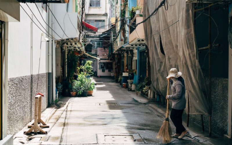 Person sweeping an alleyway on a sunny day, capturing urban life and cleanliness.