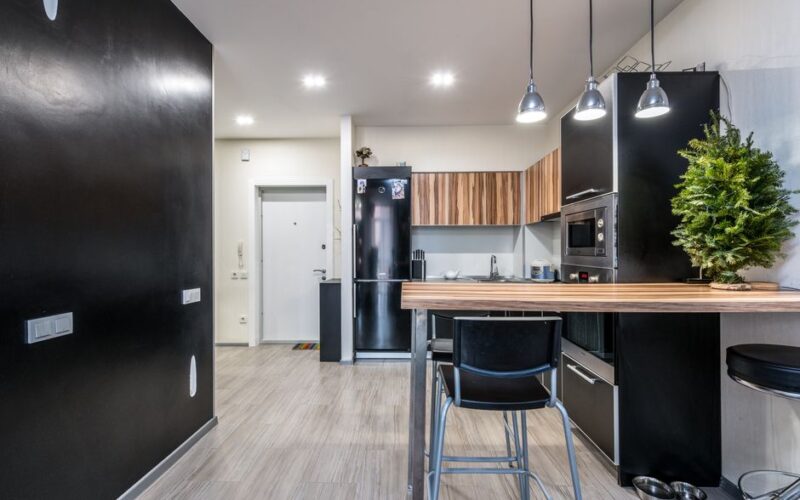Wooden counter and black cupboards in spacious kitchen with modern appliances and glowing lamps in spacious apartment