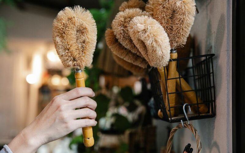 Close-up of a hand selecting eco-friendly cleaning brushes from a basket indoors.