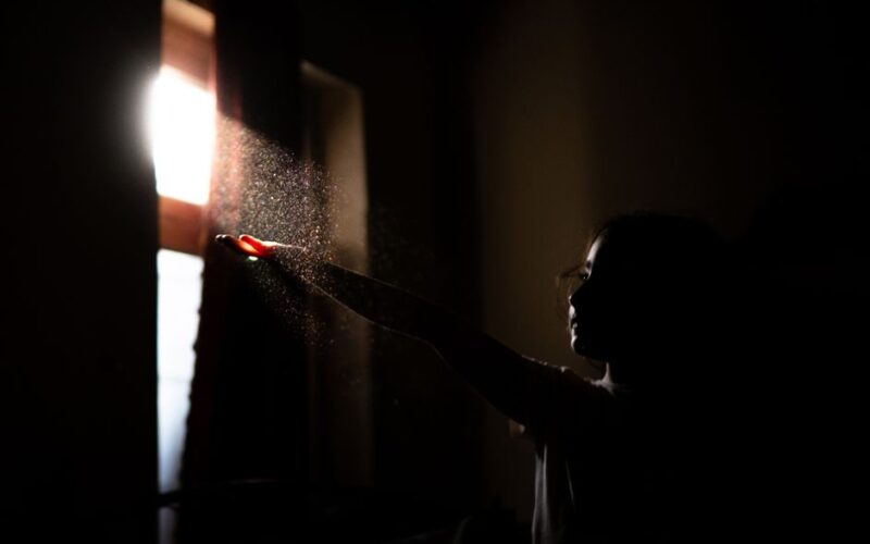 A child reaches towards sunlight through a window, illuminating dust particles.