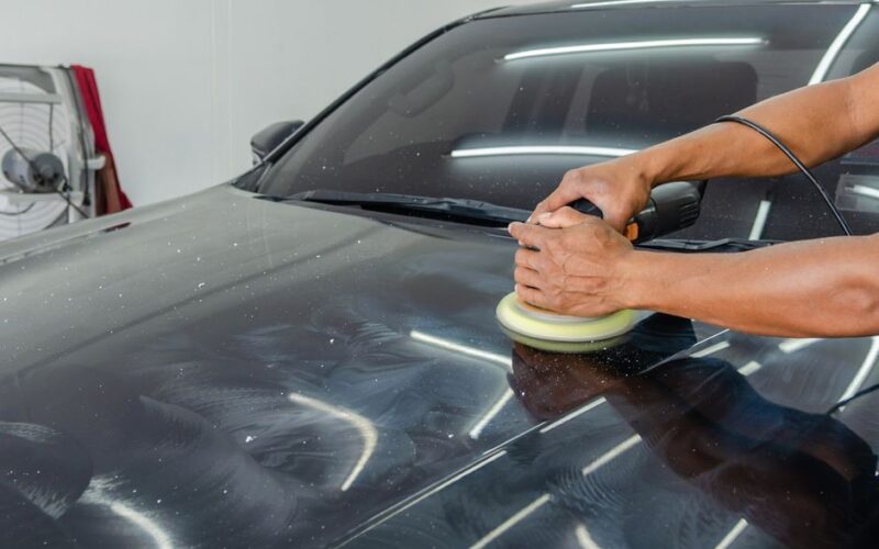 Close-up of a mechanic polishing a car's surface in an indoor auto workshop.