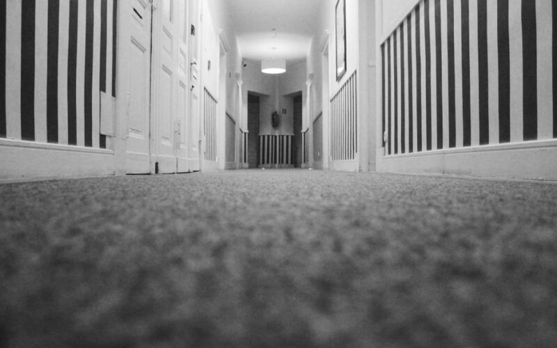 Low angle view of an empty hotel corridor with striped walls and carpet in monochrome.