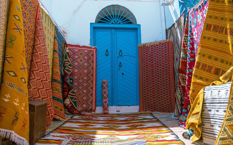 Vibrant display of traditional Tunisian carpets at a blue door entrance in Carthage, Tunisia.