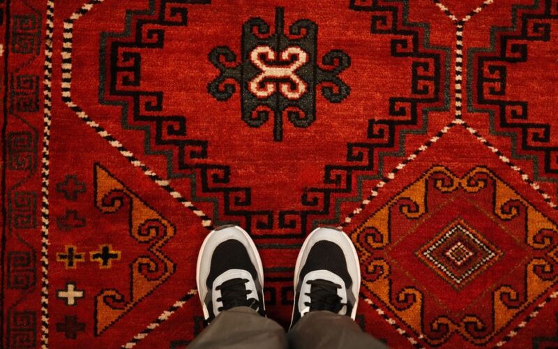 A pair of sneakers standing on a vibrant traditional red carpet in Kazakhstan.