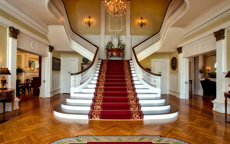 Grand staircase with red carpet in a luxurious hotel lobby, highlighted by a chandelier.