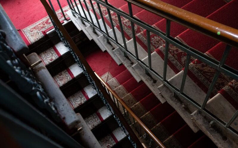 A vintage staircase with a red carpet and intricate handrail details, offering a retro perspective.