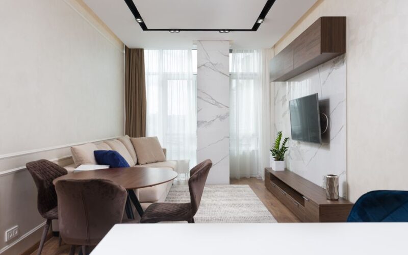 Interior of modern living living with comfortable sofa and chairs placed near round table with carpet on floor and TV on wall in modern apartment
