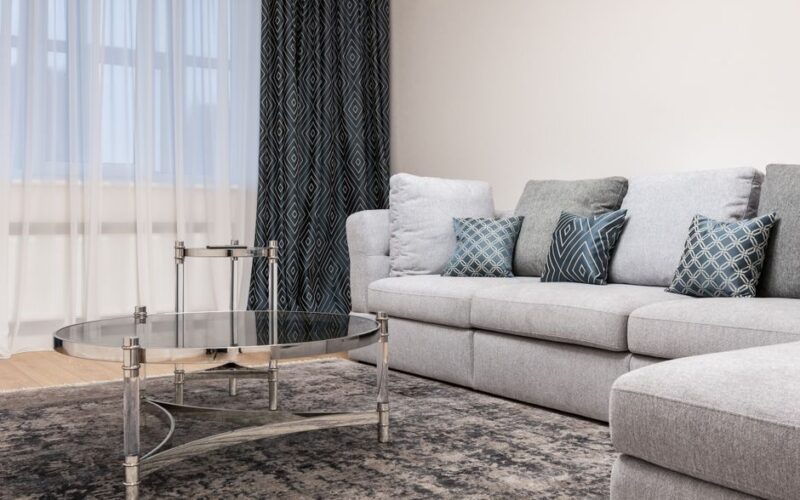 Couch with decorative cushions against metal and glass tables on rug in light house room