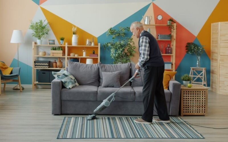 Senior man cleaning with a vacuum in a contemporary colorful living room setting.