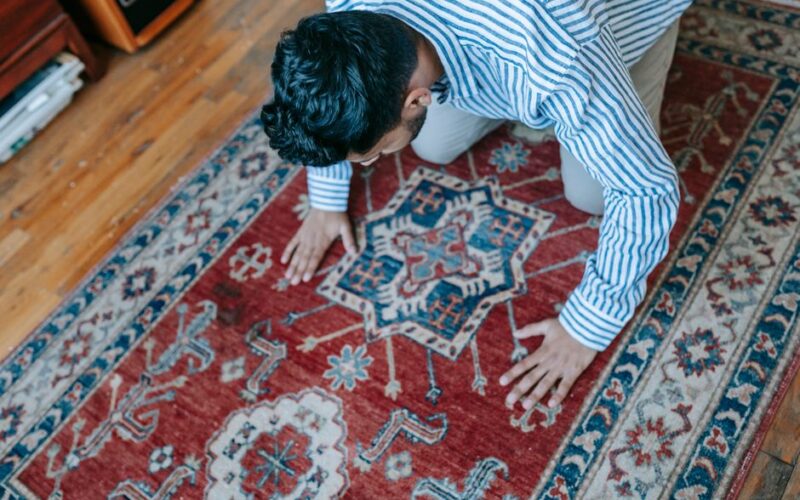 A Muslim man in prayer position on an ornate rug in a cozy indoor setting.