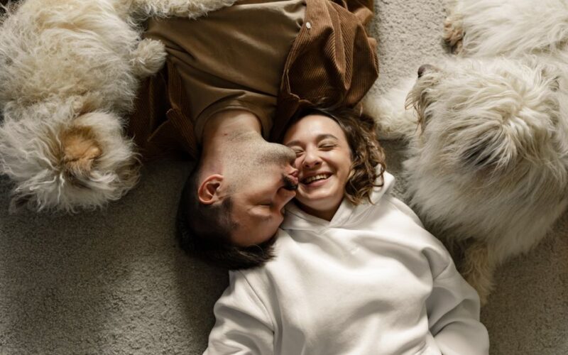 Happy couple cuddling on a carpet with two fluffy dogs, indoors and cozy.