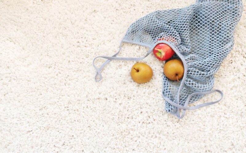 Organic apple and pears in a mesh bag resting on a textured white carpet, symbolizing freshness and sustainability.