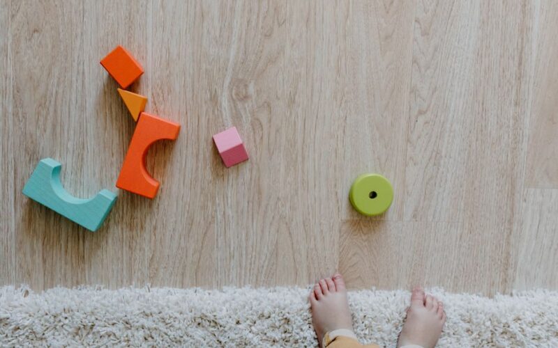 Colorful wooden blocks and baby feet on a carpet and wooden floor, emphasizing child's early playtime.