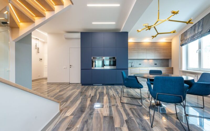 Table with armchairs on floor against cabinets and built in electric appliances in modern kitchen at home