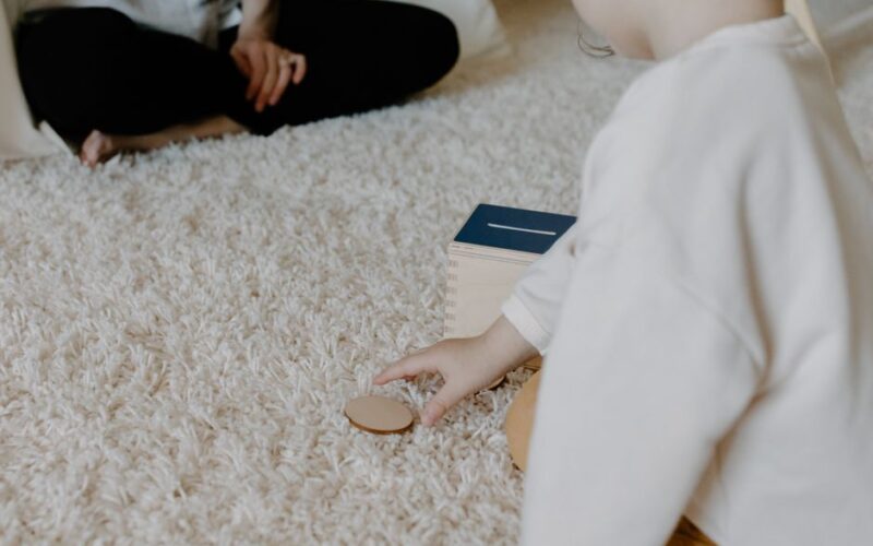 A child playing with a wooden toy on a soft carpet indoors. Minimalist and warm setting.