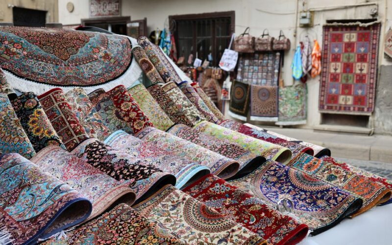 Colorful traditional rugs displayed outdoors, showcasing intricate patterns and designs in a street market.
