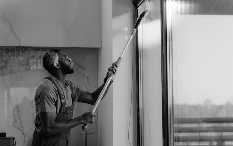 A man cleaning a glass window with a mop in grayscale, showcasing professional work.