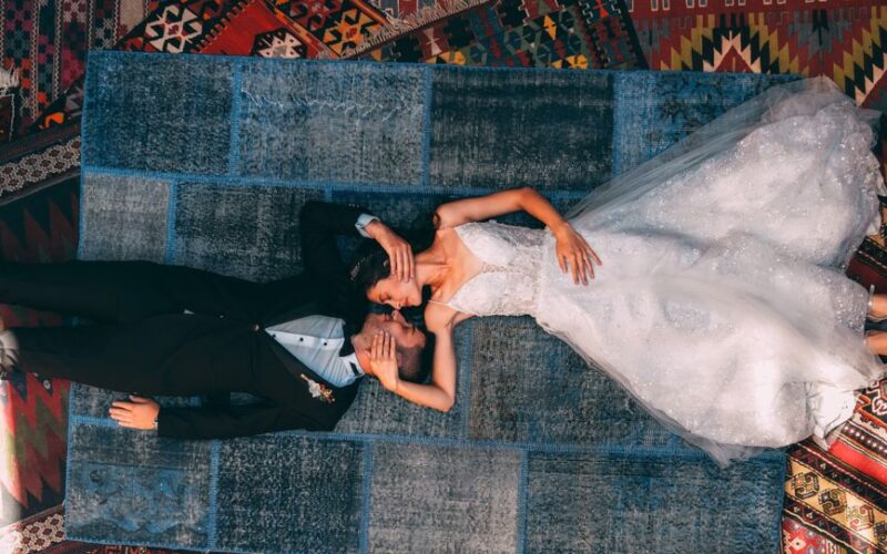 Overhead view of a newlywed couple lying on colorful carpets in Göreme, Turkey.