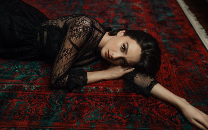 A woman in a lace dress poses elegantly on a vibrant Persian carpet.