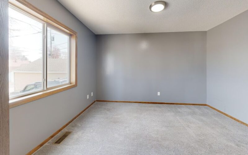 Spacious empty room with carpet, window, and neutral tones.