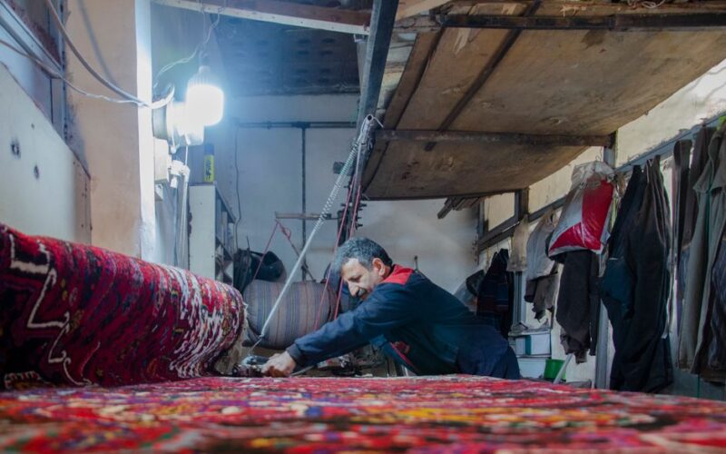 A craftsman weaving a vibrant Persian rug in a traditional workshop in Tabriz, Iran.