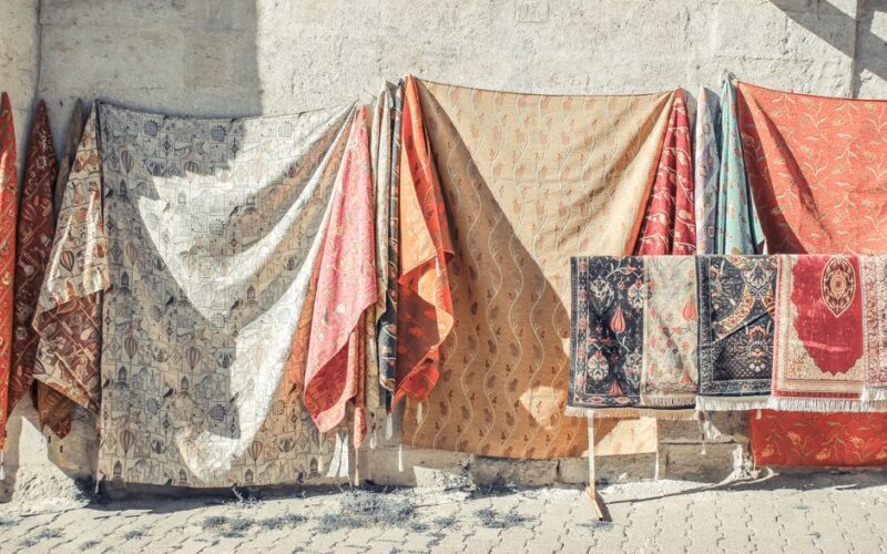 Vibrant carpets and textiles hanging outdoors in a sunlit setting, capturing cultural charm.
