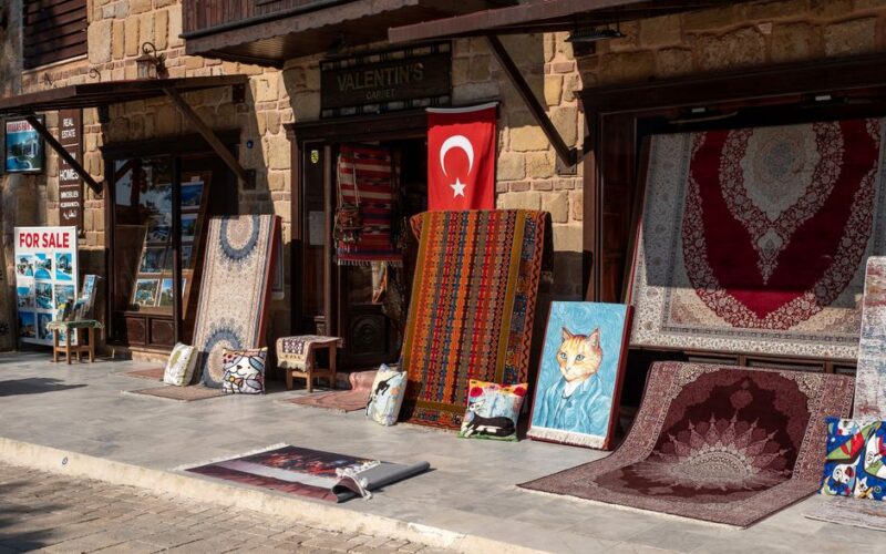 Outdoor display of various Turkish carpets and rugs in front of a store with a flag and decorative items.