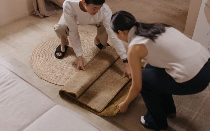 A couple rolls out a rug in a comfortable and stylish living room setting.