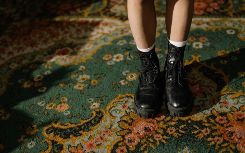 Fashionable black boots on an intricately patterned carpet in a cozy indoor setting.