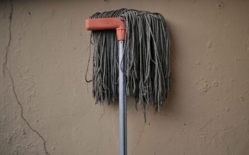 Gray mop leaning against a textured wall, conveying simplicity in a domestic setting.