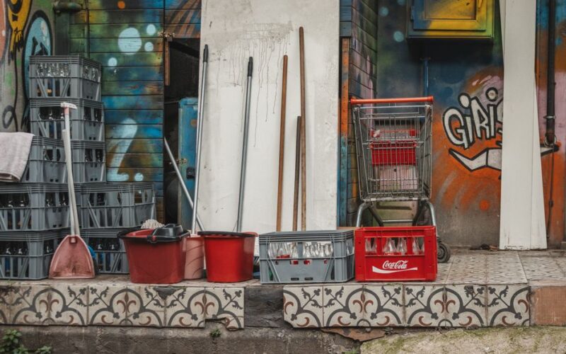 A collection of cleaning supplies and crates set against an artistic, graffiti-covered wall.