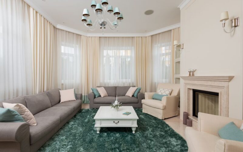 Interior of classic living room with gray sofas and beige armchair on soft carpet near stone fireplace under chandelier