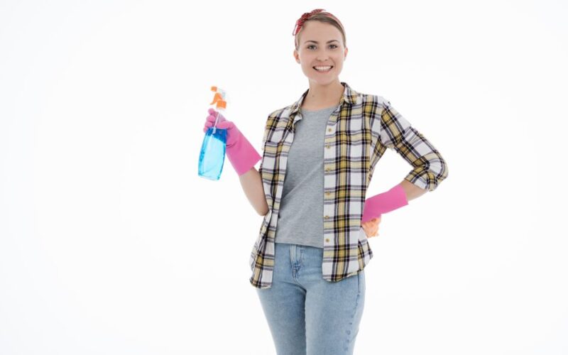 Smiling woman in plaid shirt and latex gloves holding cleaning spray on white background.