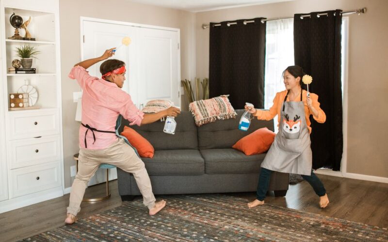 A joyful couple engages in a playful cleaning fight in their living room, showcasing light-hearted domestic life.