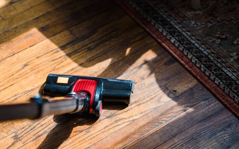 Close-up of a vacuum cleaner on wooden flooring near a patterned rug, showcasing domestic cleaning.
