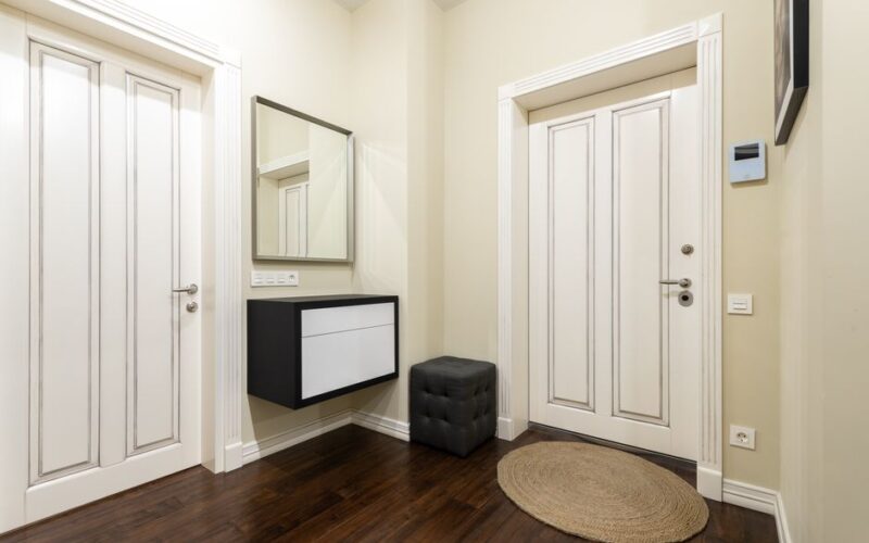 Contemporary corridor interior with carpet and pouf on parquet under cabinet and mirror between doors at home