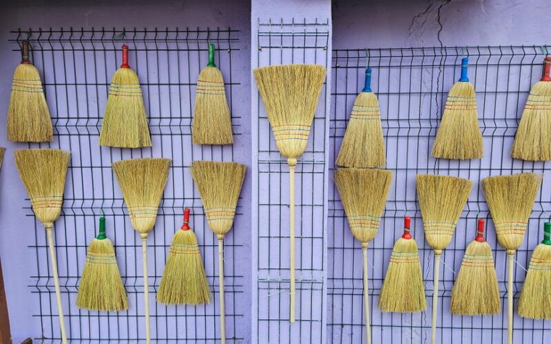 Vibrant brooms with colored handles hanging on a purple wall for a rustic decor touch.