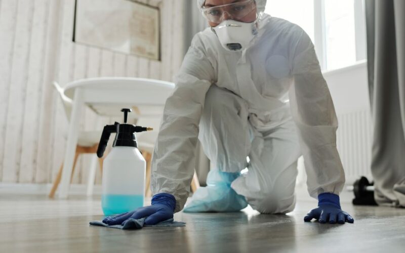 Person in protective suit cleaning a floor indoors to prevent virus spread.