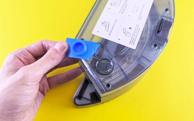 Close-up of a person holding a vacuum cleaner water tank with a yellow background.