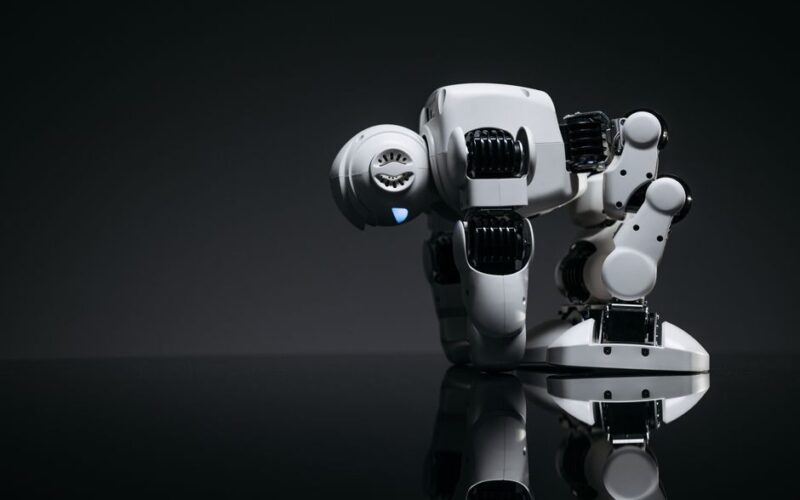 A modern robot toy depicted in a studio environment with its reflection visible on a dark surface.