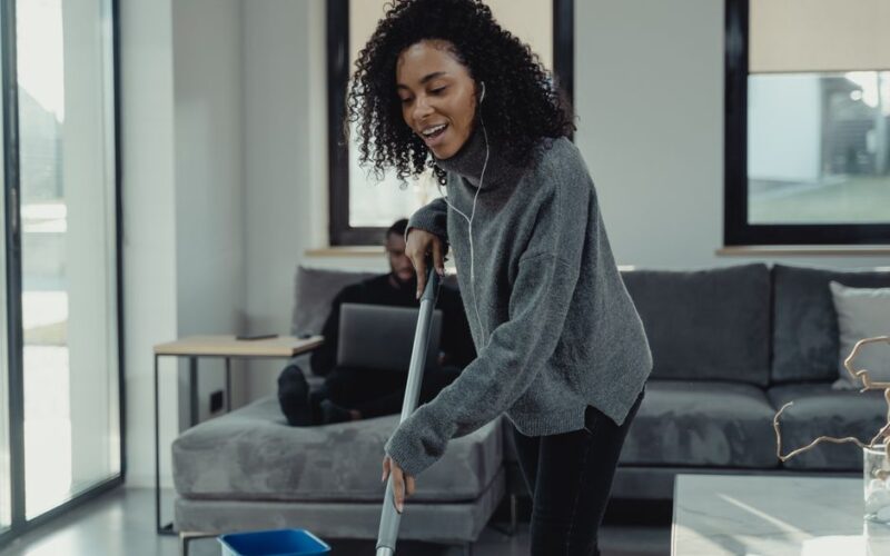 A cheerful young woman mopping the floor in a cozy, modern living room.