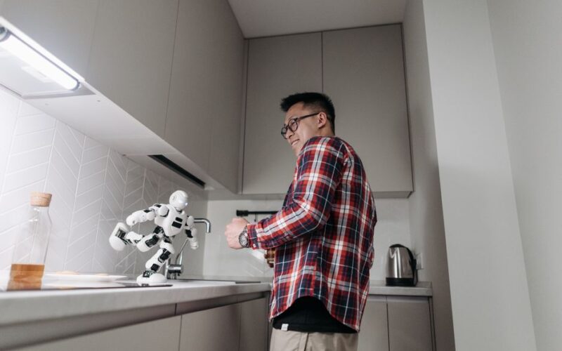Asian man smiling while playing with a robot in a modern kitchen setting.