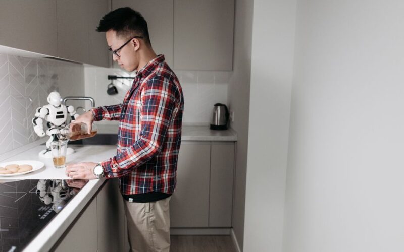 Man in plaid shirt pours drink in a sleek kitchen with a robot.